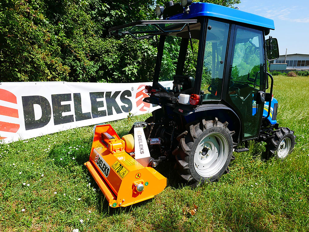 Compact tractor with DELEKS APE flail mower cutting grass on a slope