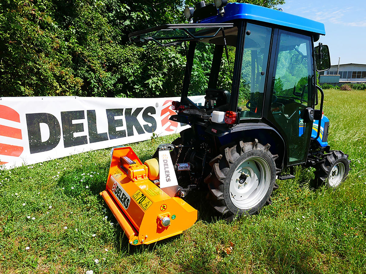 Compact tractor with DELEKS APE flail mower cutting grass on a slope
