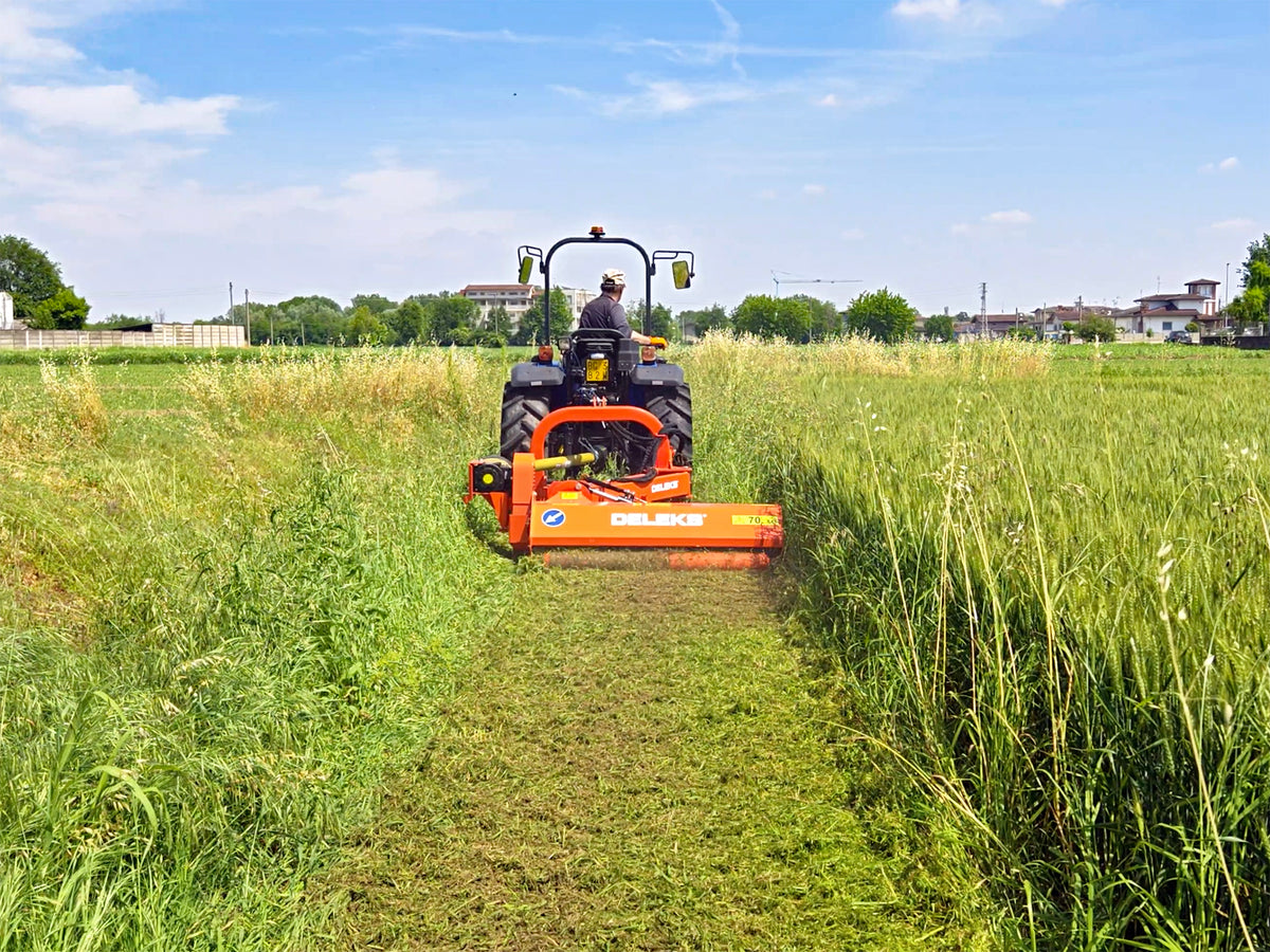 Tractor cutting tall grass in a field with the DELEKS GIRAFFA flail mower